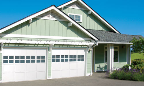 new white wood garage door on green home